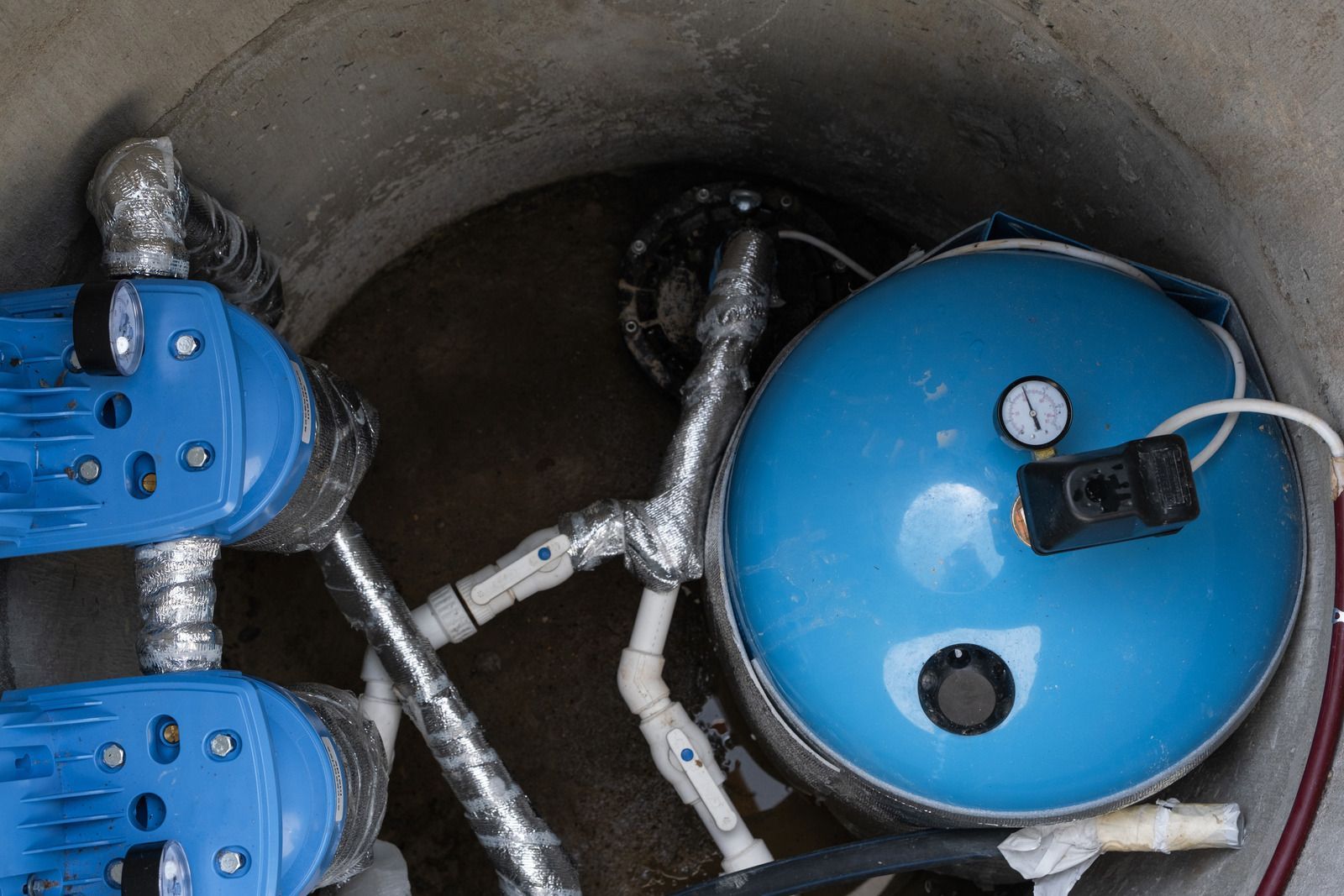 Blue pressure tank and pipes inside a circular utility chamber