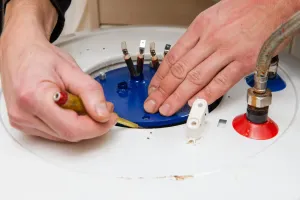 Hands using a screwdriver to work on a white water heater with blue and red fittings