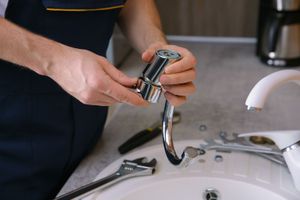 Person attaching a chrome faucet sprayer in a bathroom sink.