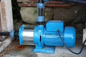 Blue electric water pump connected to pipes beside a brick wall on a concrete floor