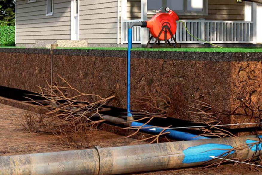 Cutaway of a yard showing plumbing and a machine clearing a pipe. Brown soil, blue pipes, orange machine.