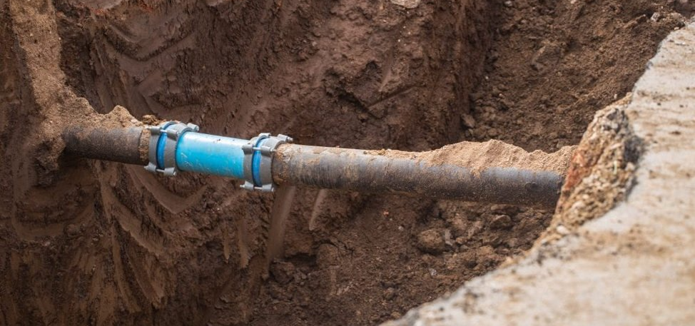 A water linepipe is sitting in the dirt in a hole.