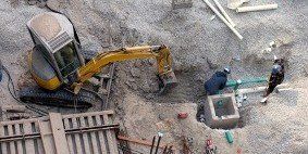 An aerial view of a construction site with a yellow excavator replacing a sewer line
