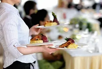 A waitress is carrying two plates of food to a table.