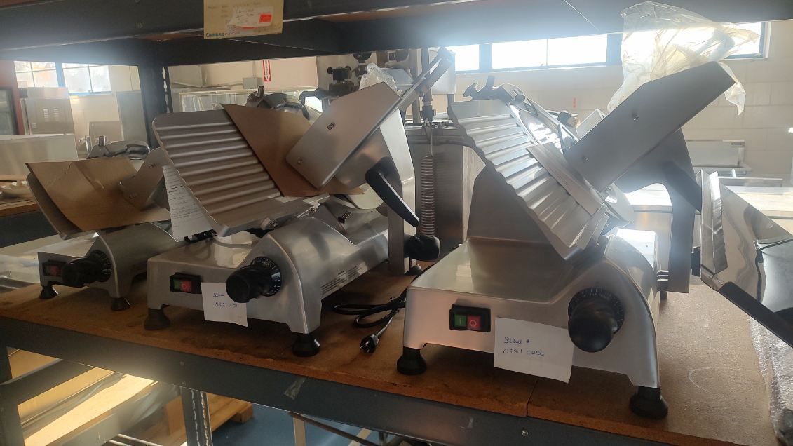 A row of meat slicers sitting on top of a wooden shelf.