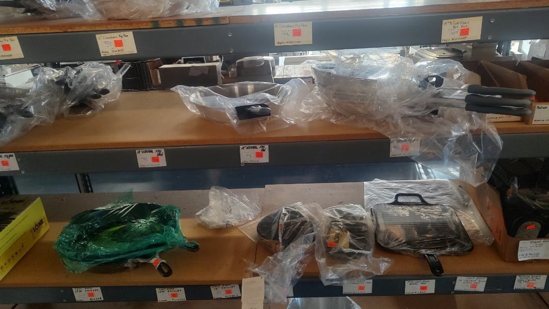 A shelf filled with lots of pots and pans wrapped in plastic.