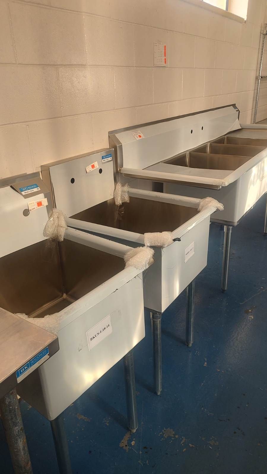 A row of stainless steel sinks are lined up in a room.