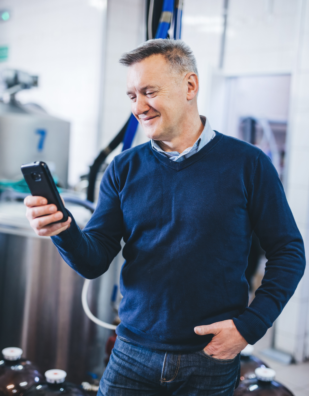 A man in a blue sweater is holding a cell phone in his hand.