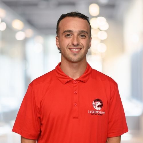 Man in a red polo shirt smiling, Lexington logo on shirt, in an office setting.