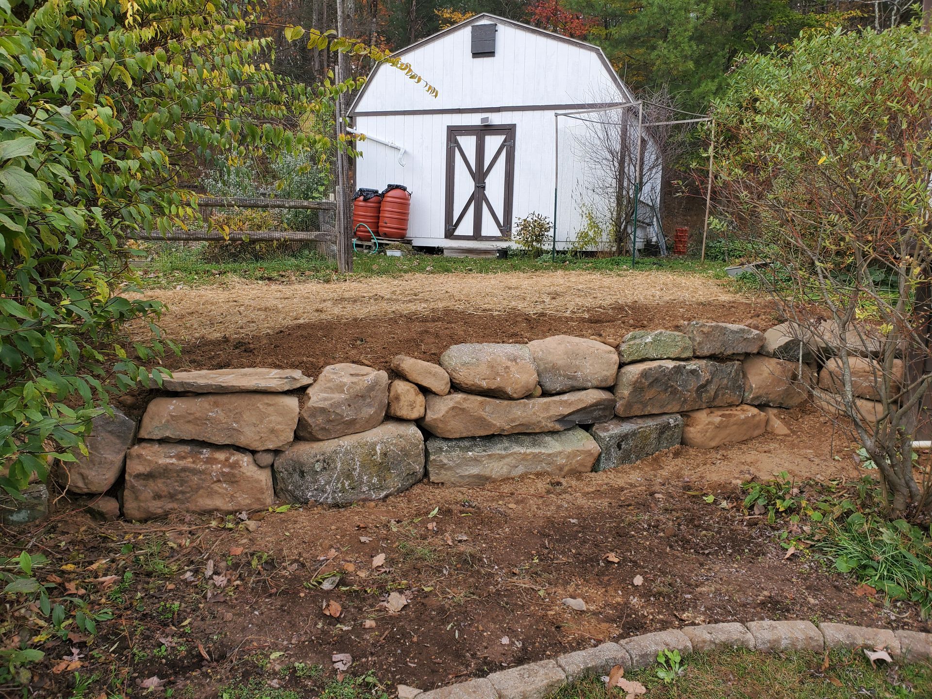 A stone wall is being built in front of a white barn.