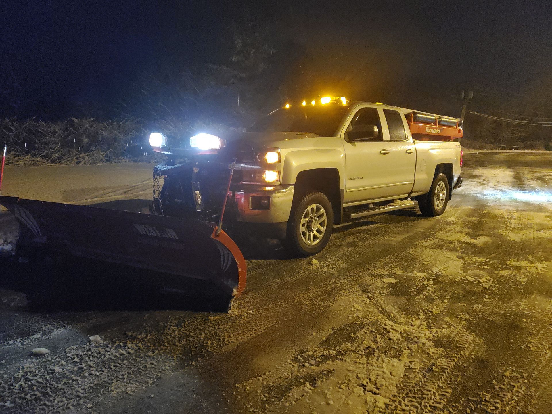 A truck with a snow plow attached to it is parked in a parking lot at night.