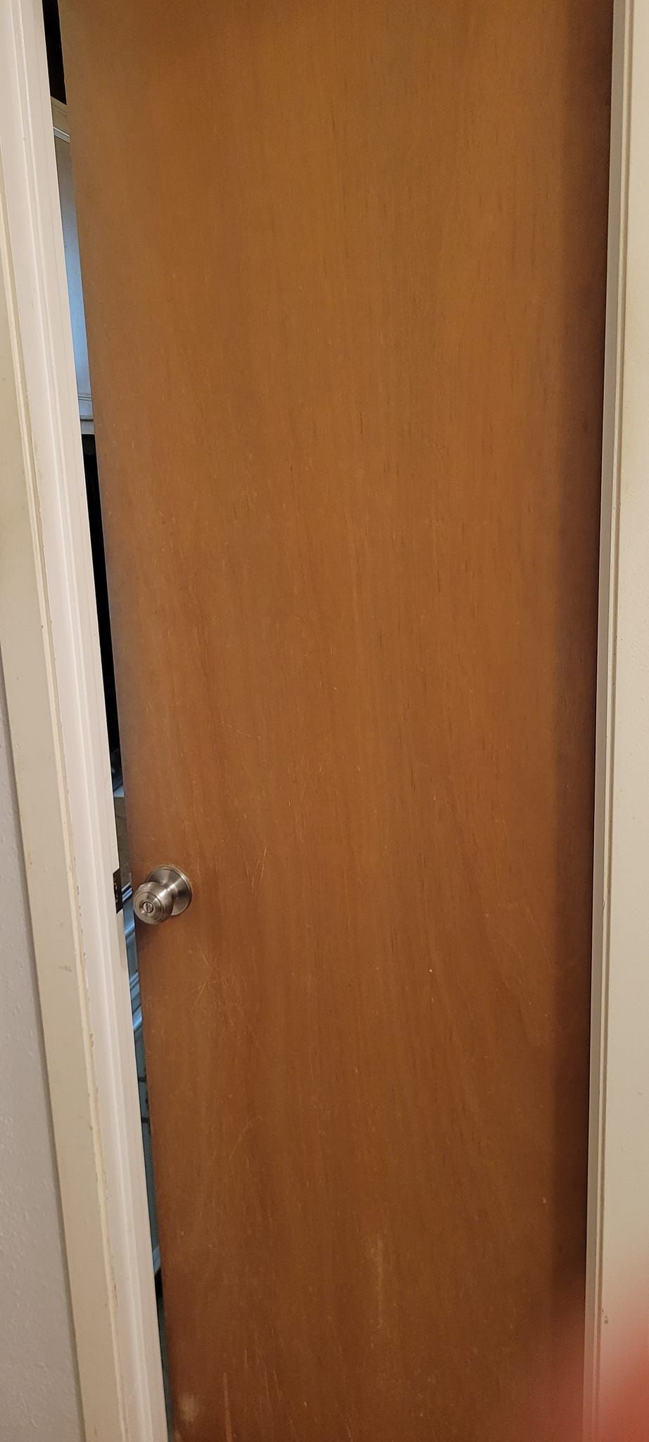 A slightly open brown door with a silver handle, framed by white trim.