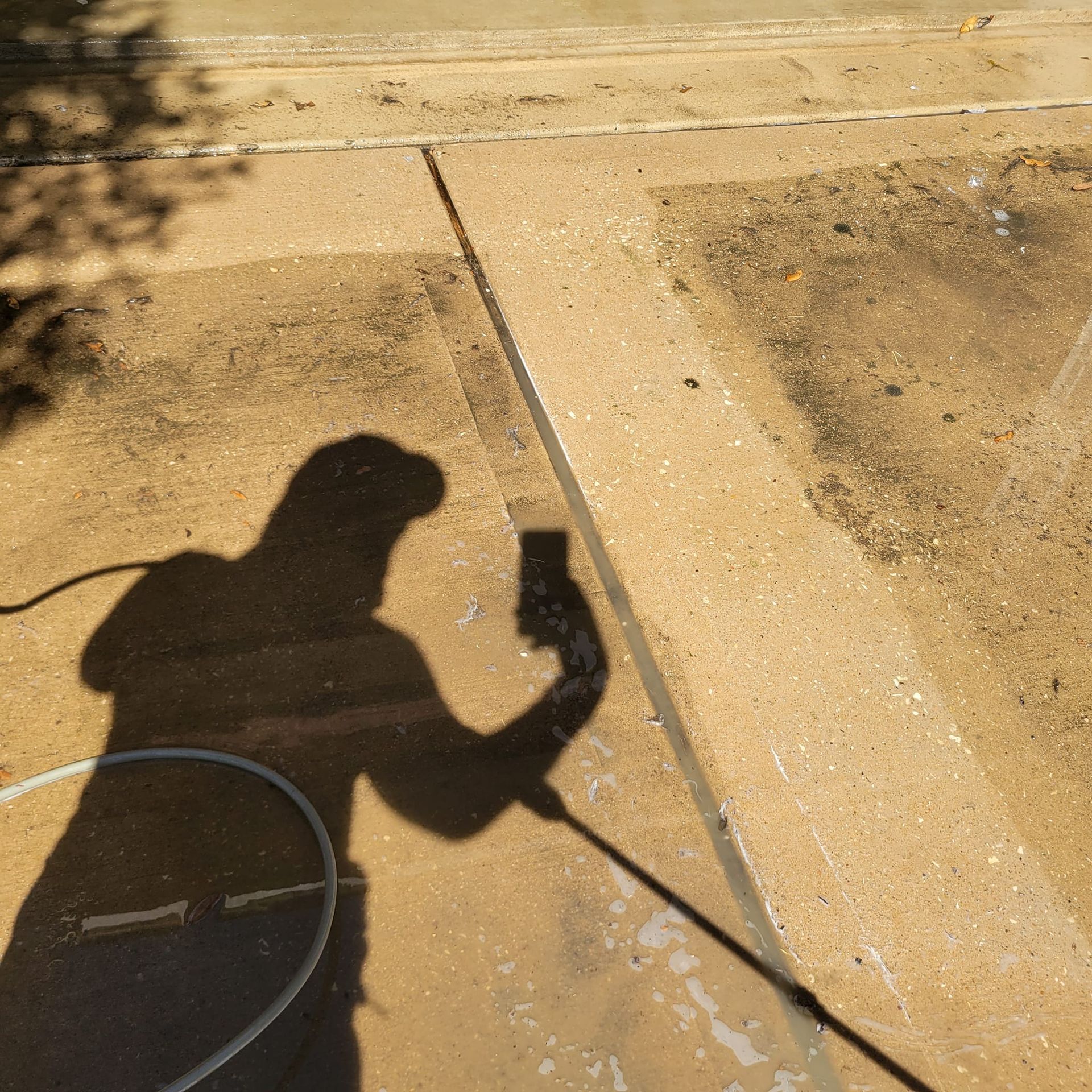 Shadow of person pressure washing a tan concrete surface outdoors.
