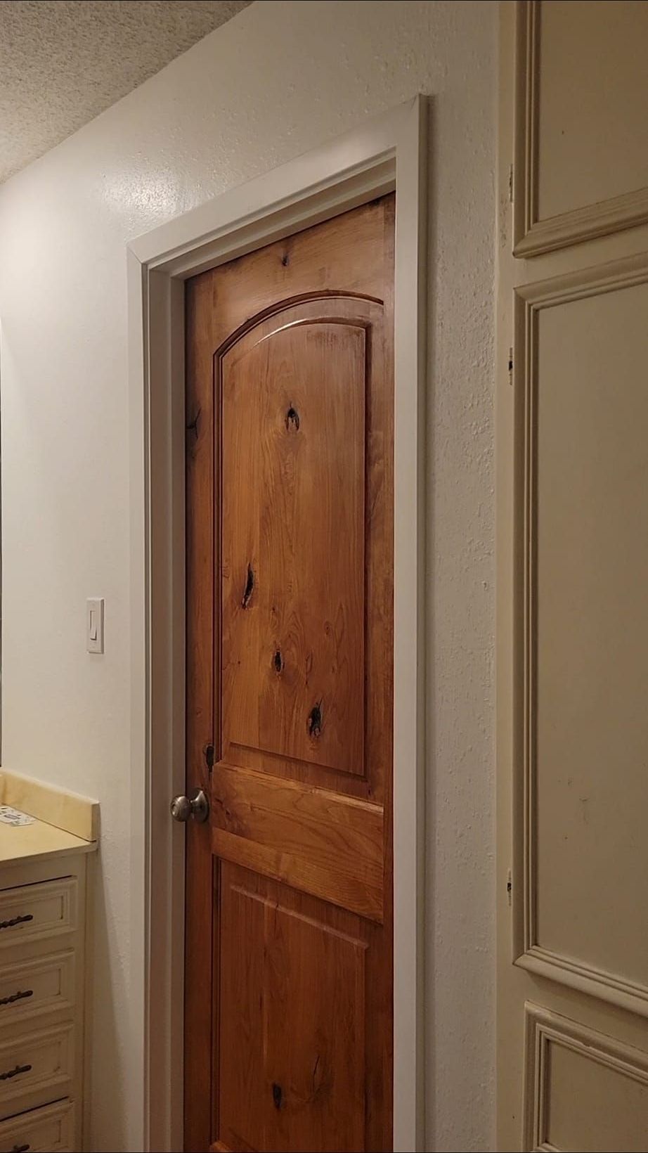 A wooden door with a curved top and silver doorknob, set in a white-trimmed frame in a bathroom.