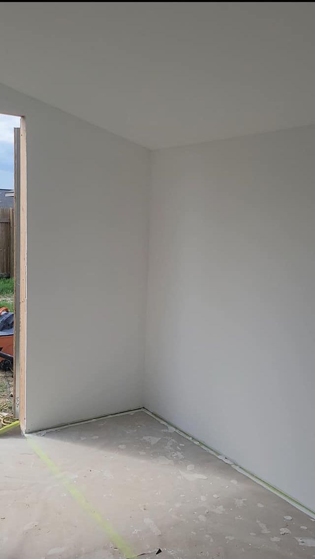 Corner of an unfinished room with white walls and a concrete floor, an open doorway on the left, outdoor view.