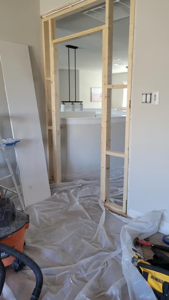 Interior doorway under construction: Wooden frame, plastic sheeting on floor, and tools are visible. 