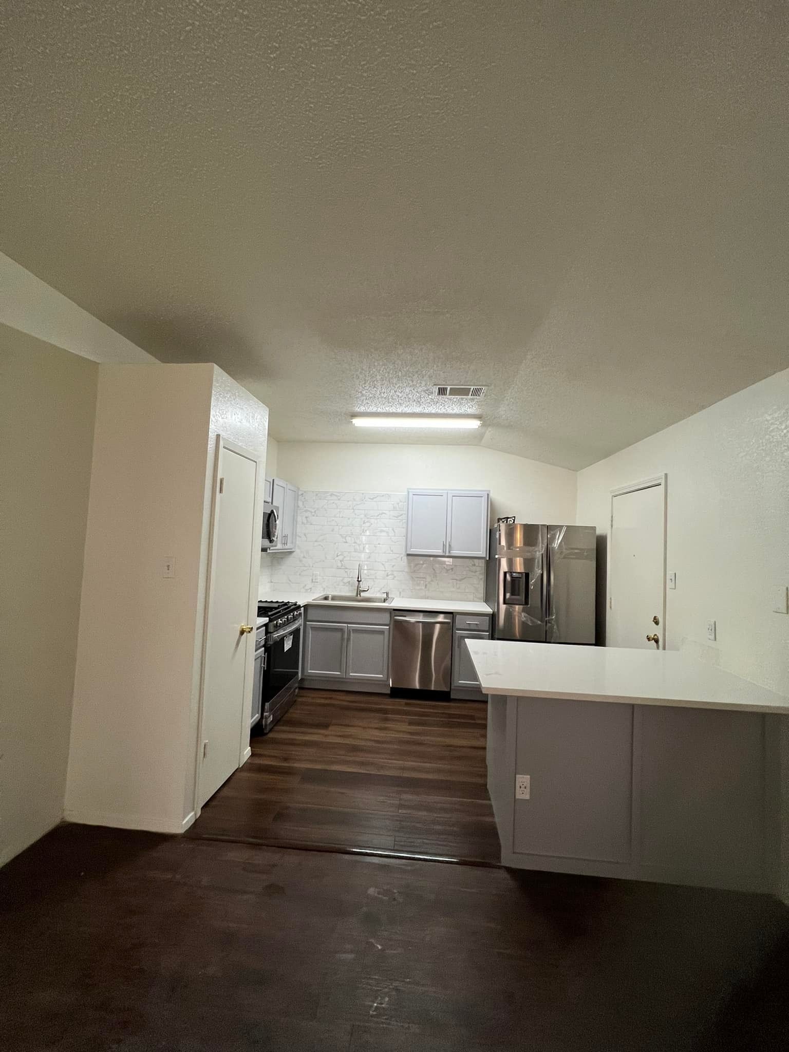 A kitchen with stainless steel appliances, grey cabinets, a white tile backsplash, 