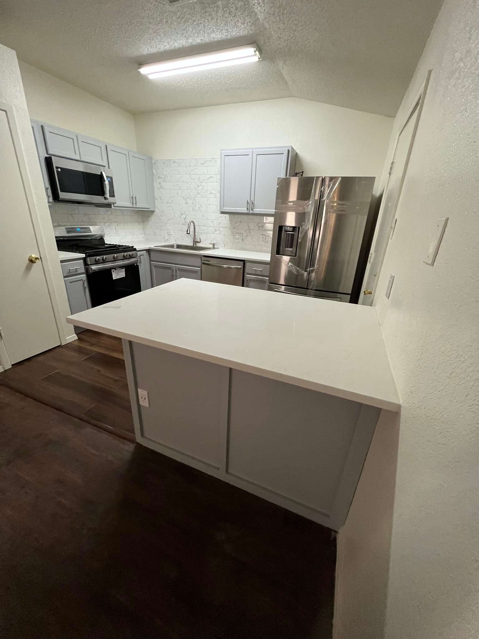 Kitchen with gray cabinets, stainless steel appliances, and a white countertop island.