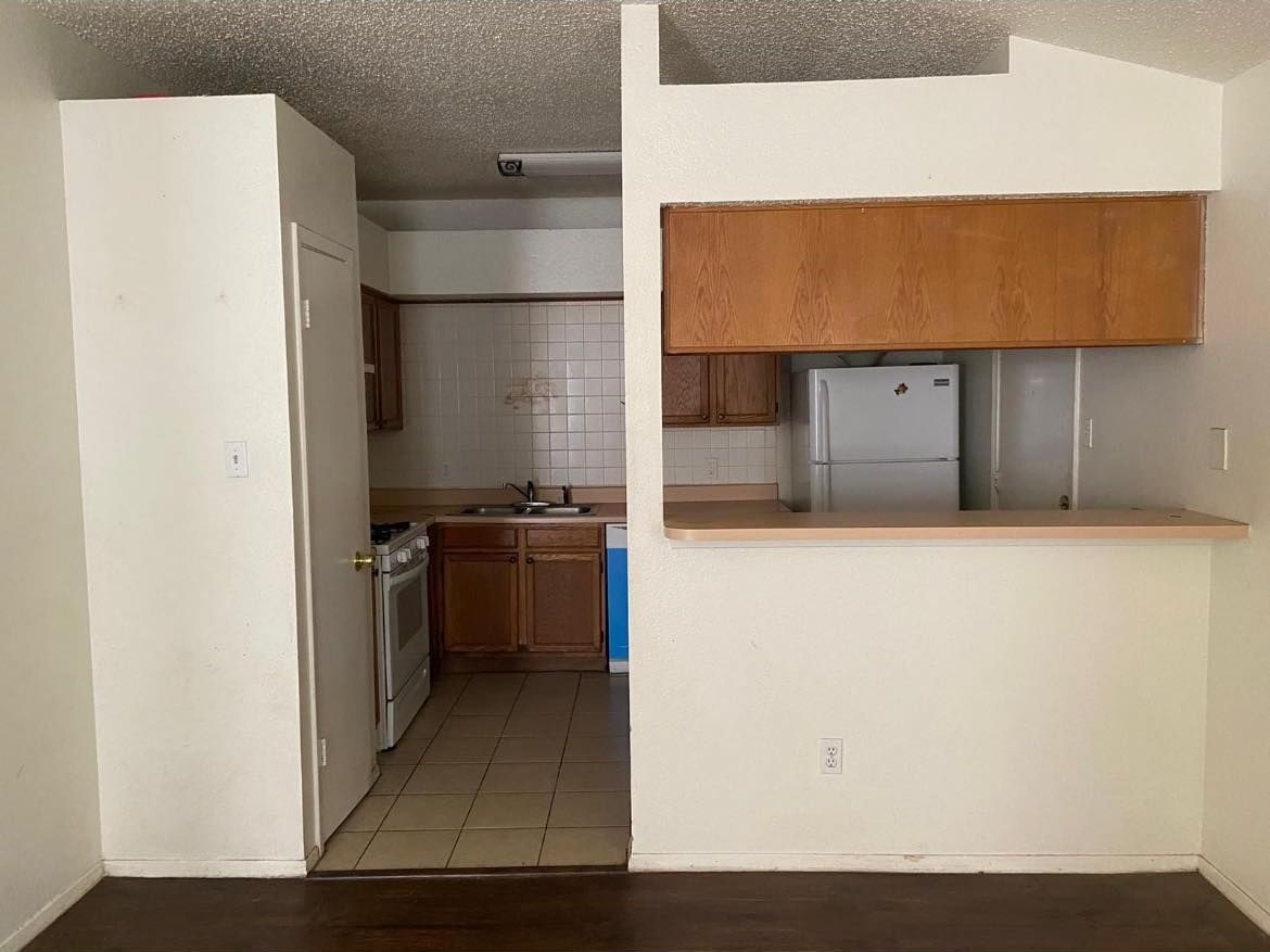 An interior view of a kitchen with a partial wall separating it from a living area. The 