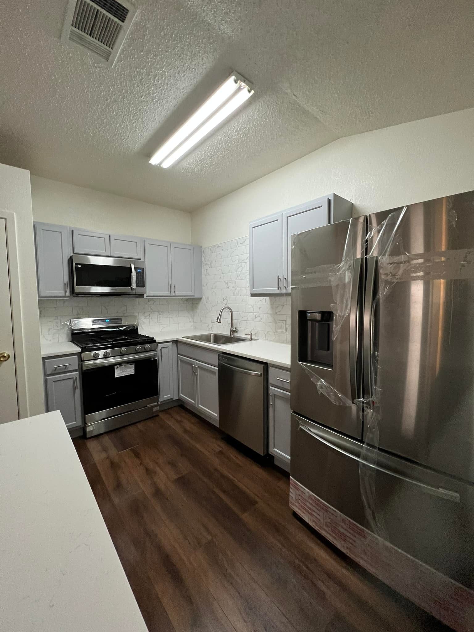 Kitchen with gray cabinets, stainless steel appliances, white countertop, and dark wood flooring.