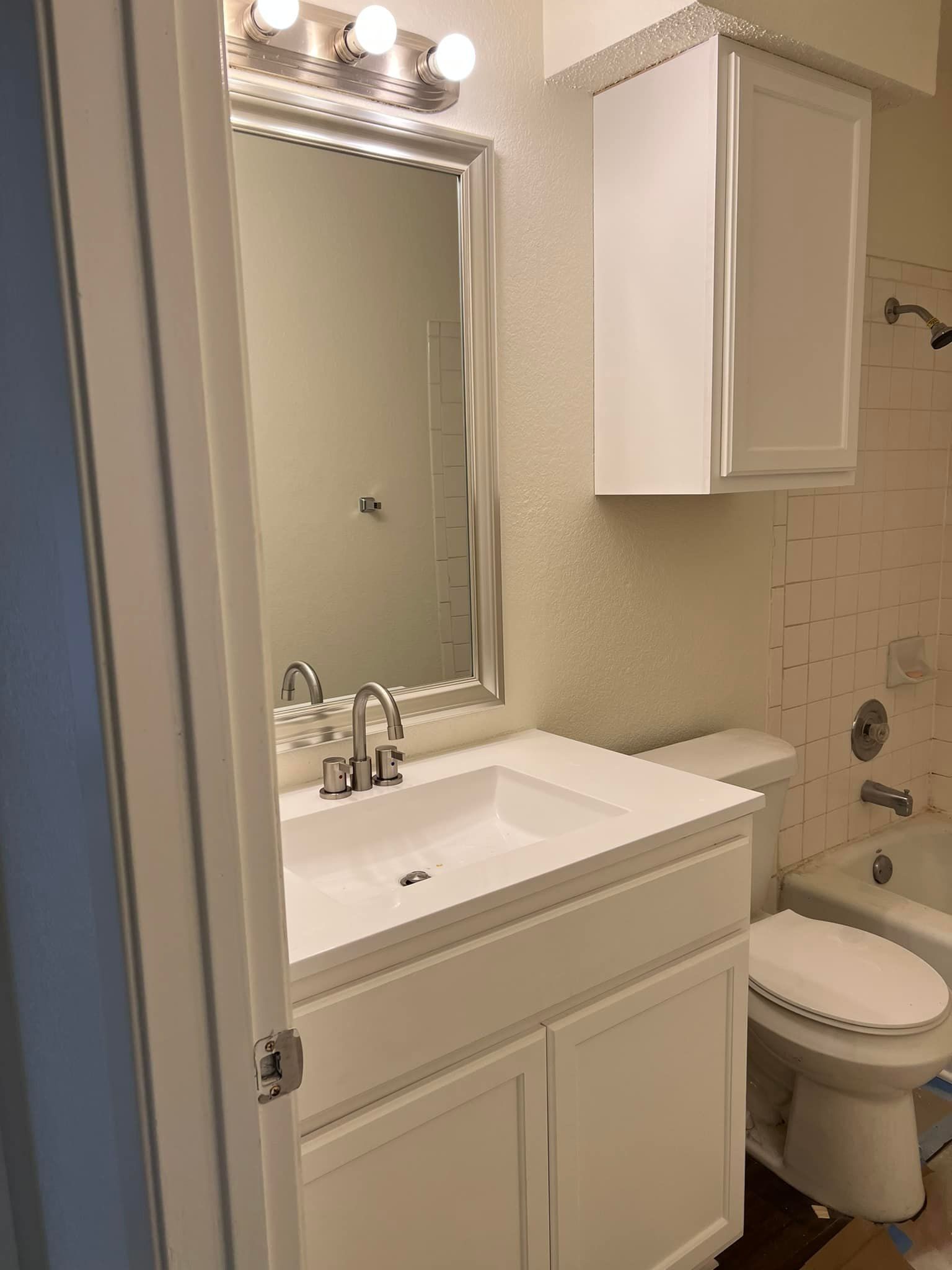 White bathroom with a vanity, mirror, overhead cabinet, and toilet.