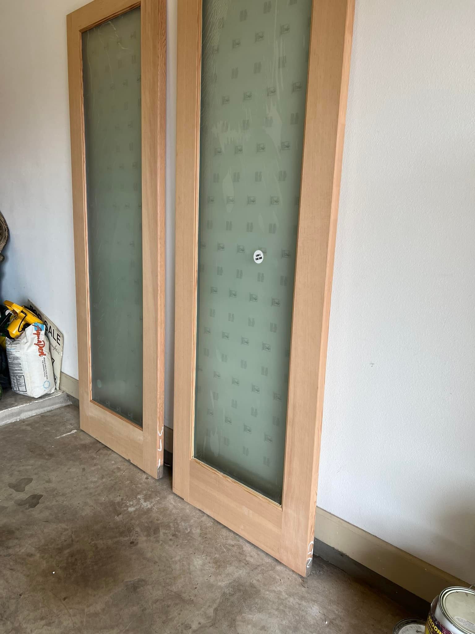 Two wooden doors with frosted glass panels, leaning against a white wall in a garage.
