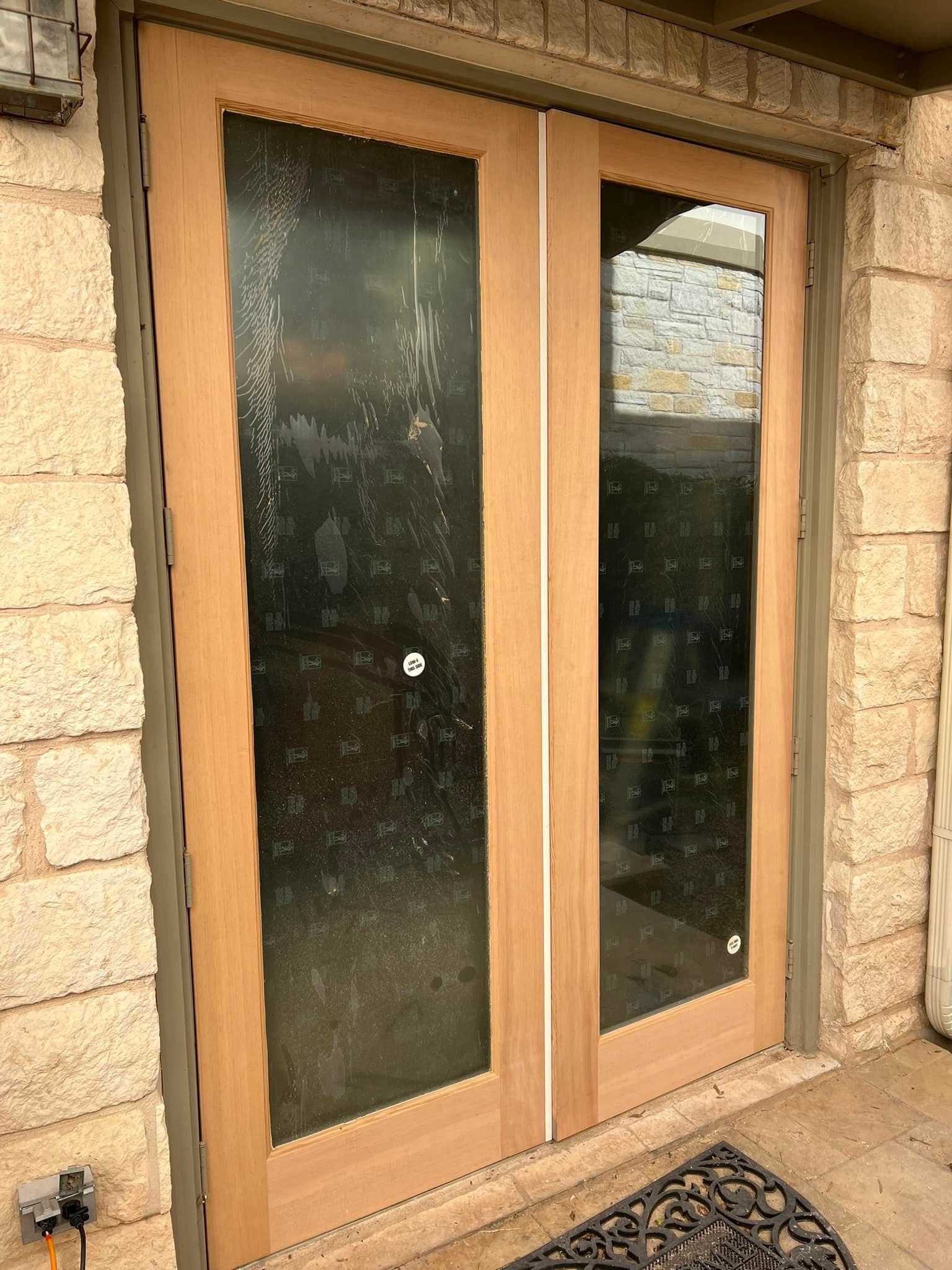 Two wooden double doors with large glass panels, set in a stone building. The glass is covered in smudges and marks.
