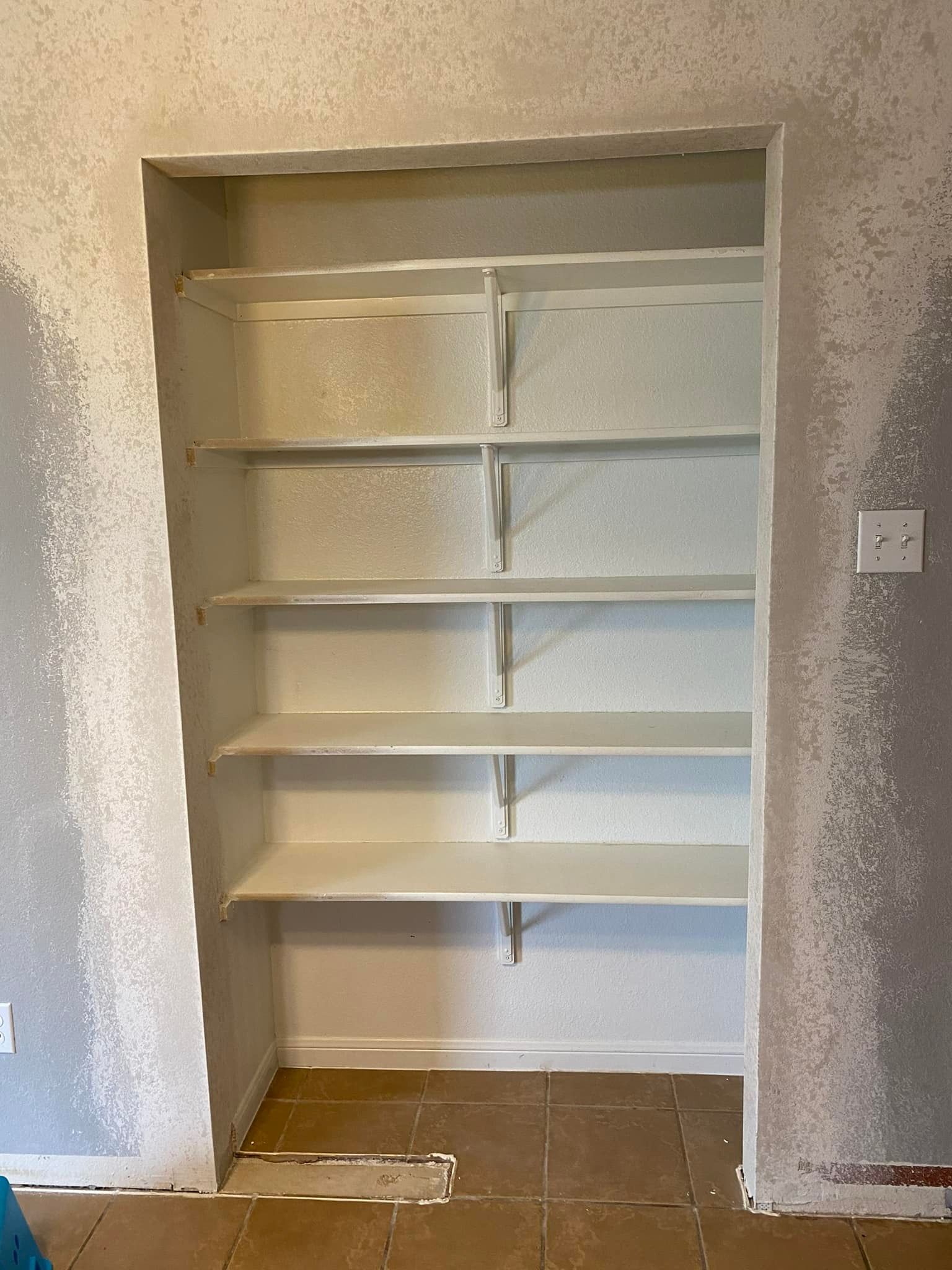 Built-in shelving unit in a wall niche, painted white, with a light grey wall texture.