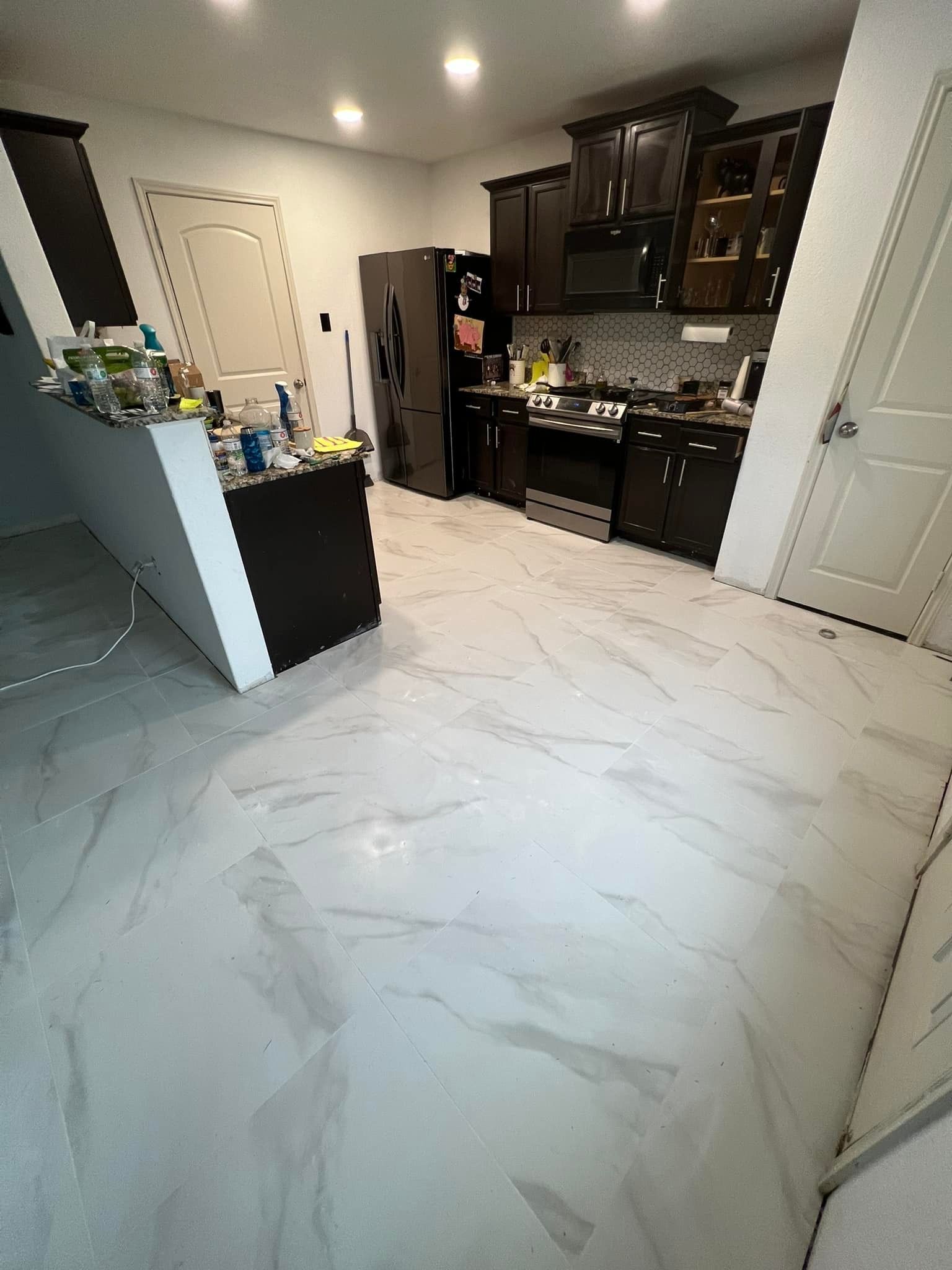 A modern kitchen with white marble flooring, dark cabinets, and stainless steel appliances.