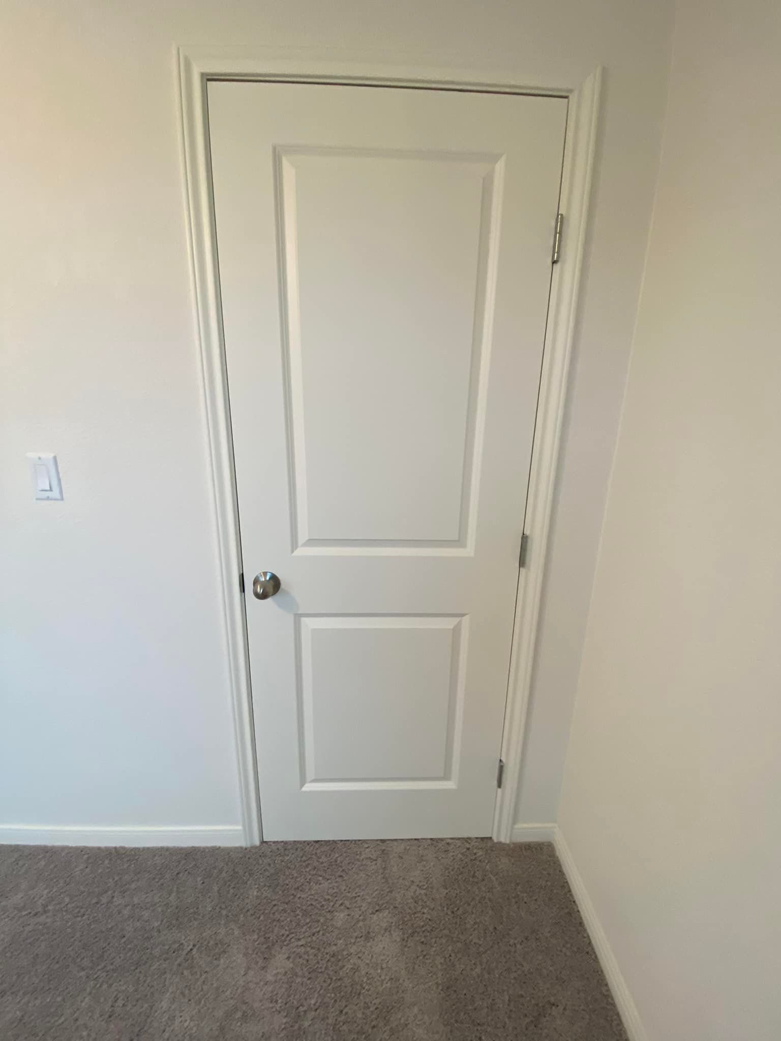 A white door with a silver doorknob set in a white door frame, with white walls and brown carpet.