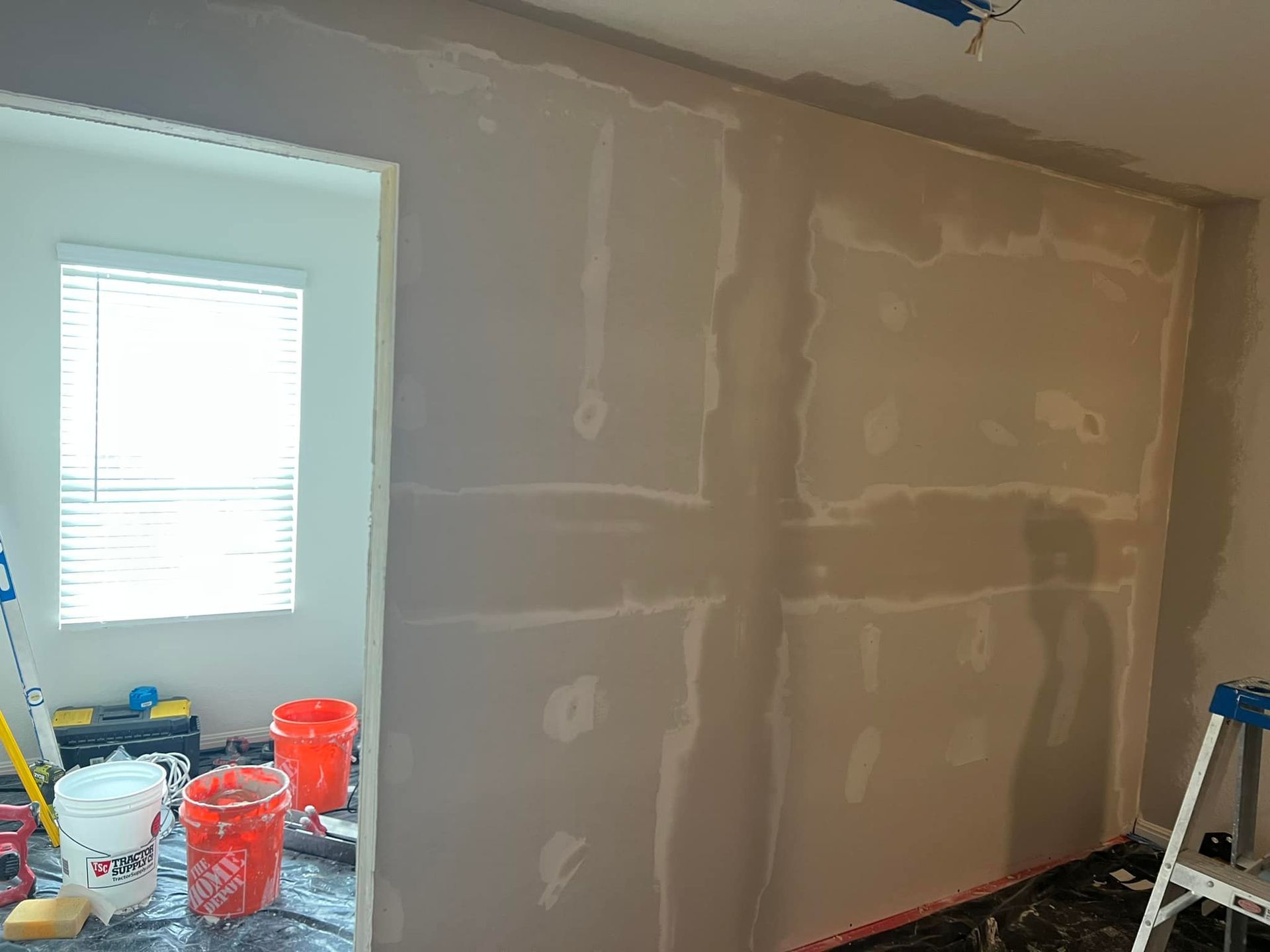 Interior view of a room with drywall installed on the walls; buckets and tools are in the foreground, & a window is visible.