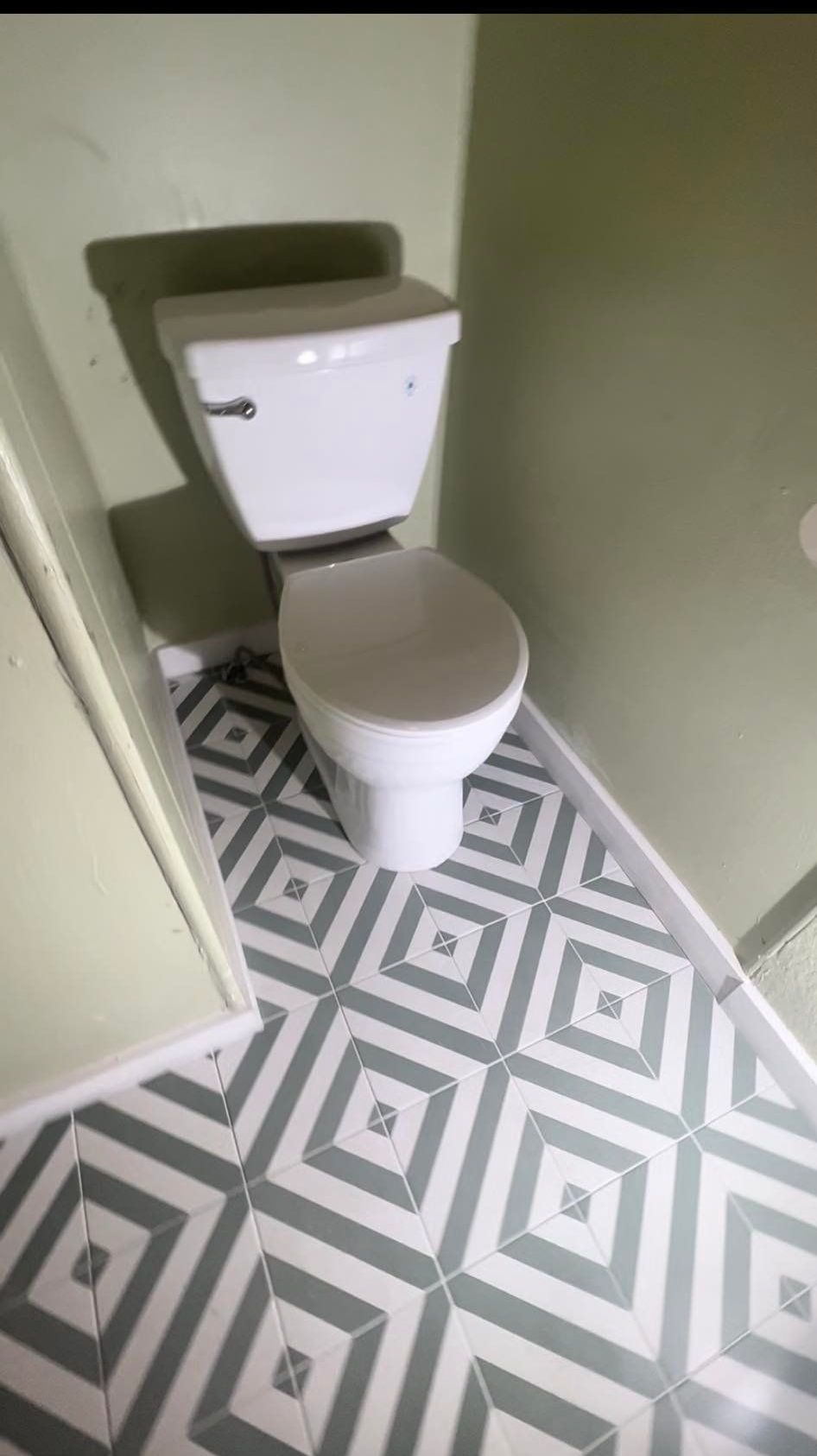 Toilet in a small bathroom with geometric tile flooring, light green walls, and white trim.