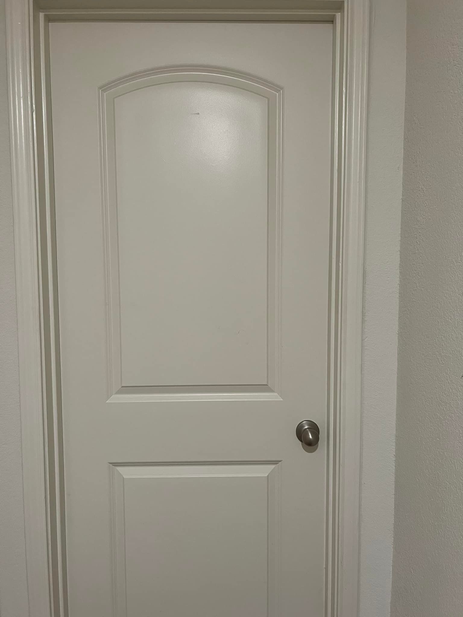 White interior door with silver doorknob, set in a white frame against a textured wall.