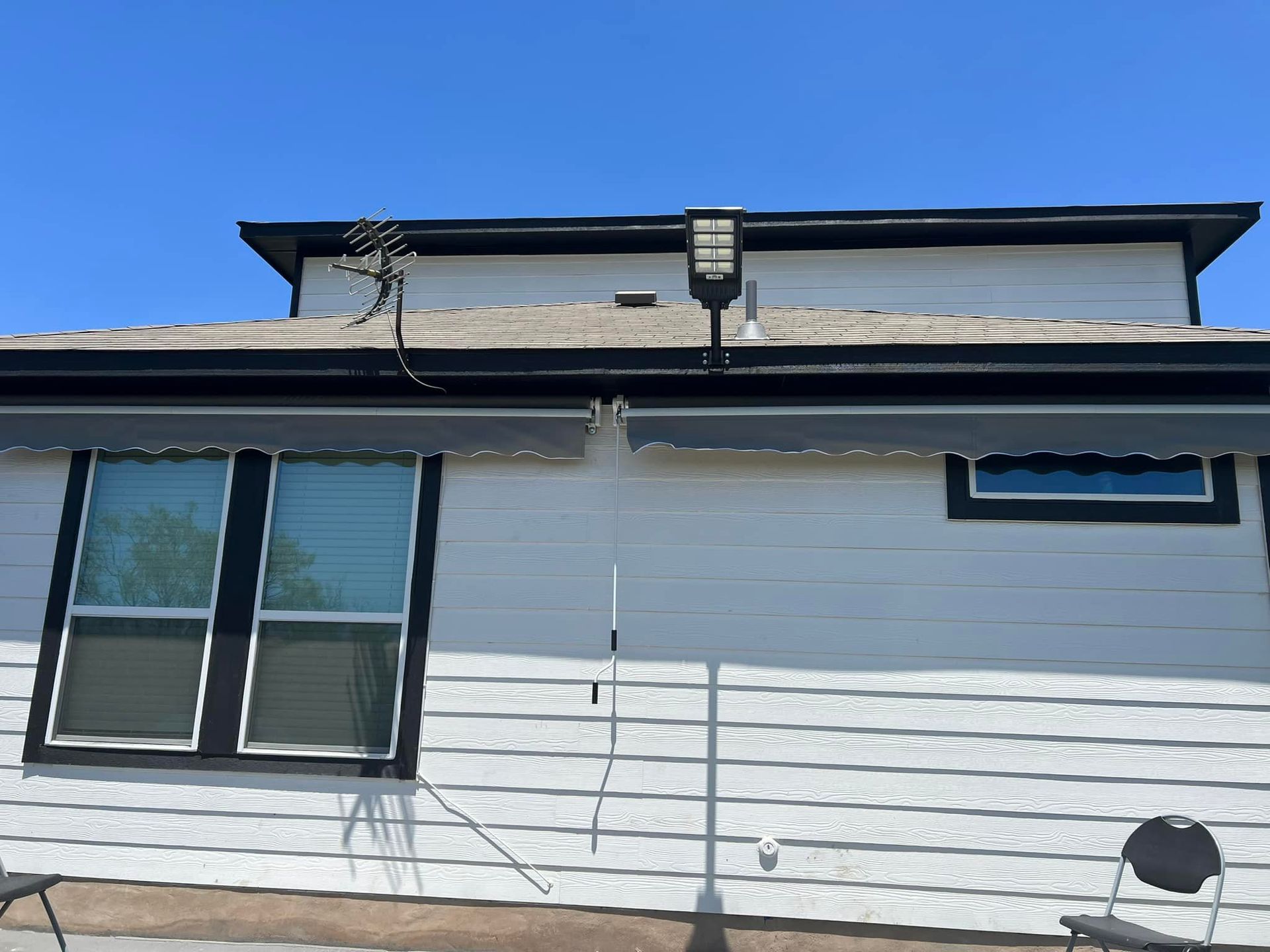 White house exterior with black trim and awning; satellite dish on the roof. Blue sky overhead.
