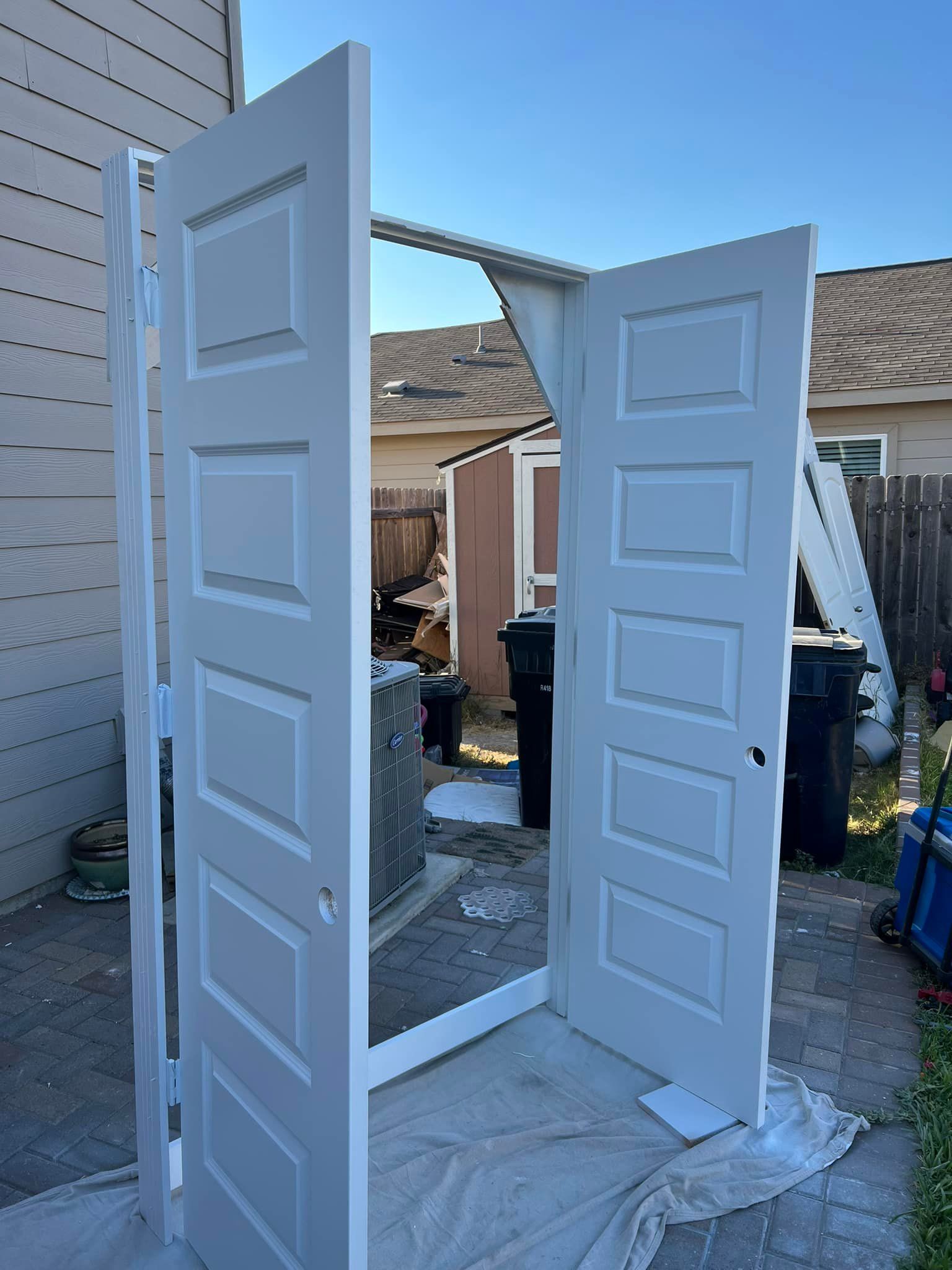 Two white paneled doors propped open in an outdoor setting. 