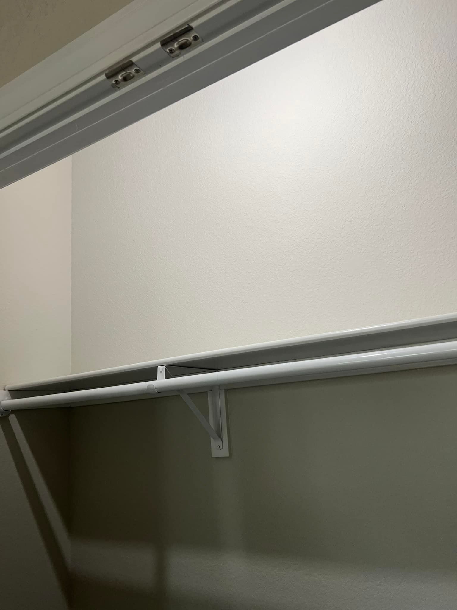 Empty white closet with a shelf and rod installed. The walls are a light beige color.