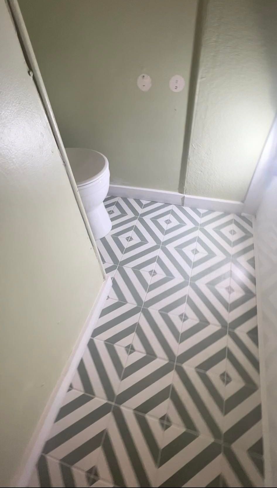 Overhead view of a small bathroom with geometric patterned floor tiles, a white toilet, and pale green walls.