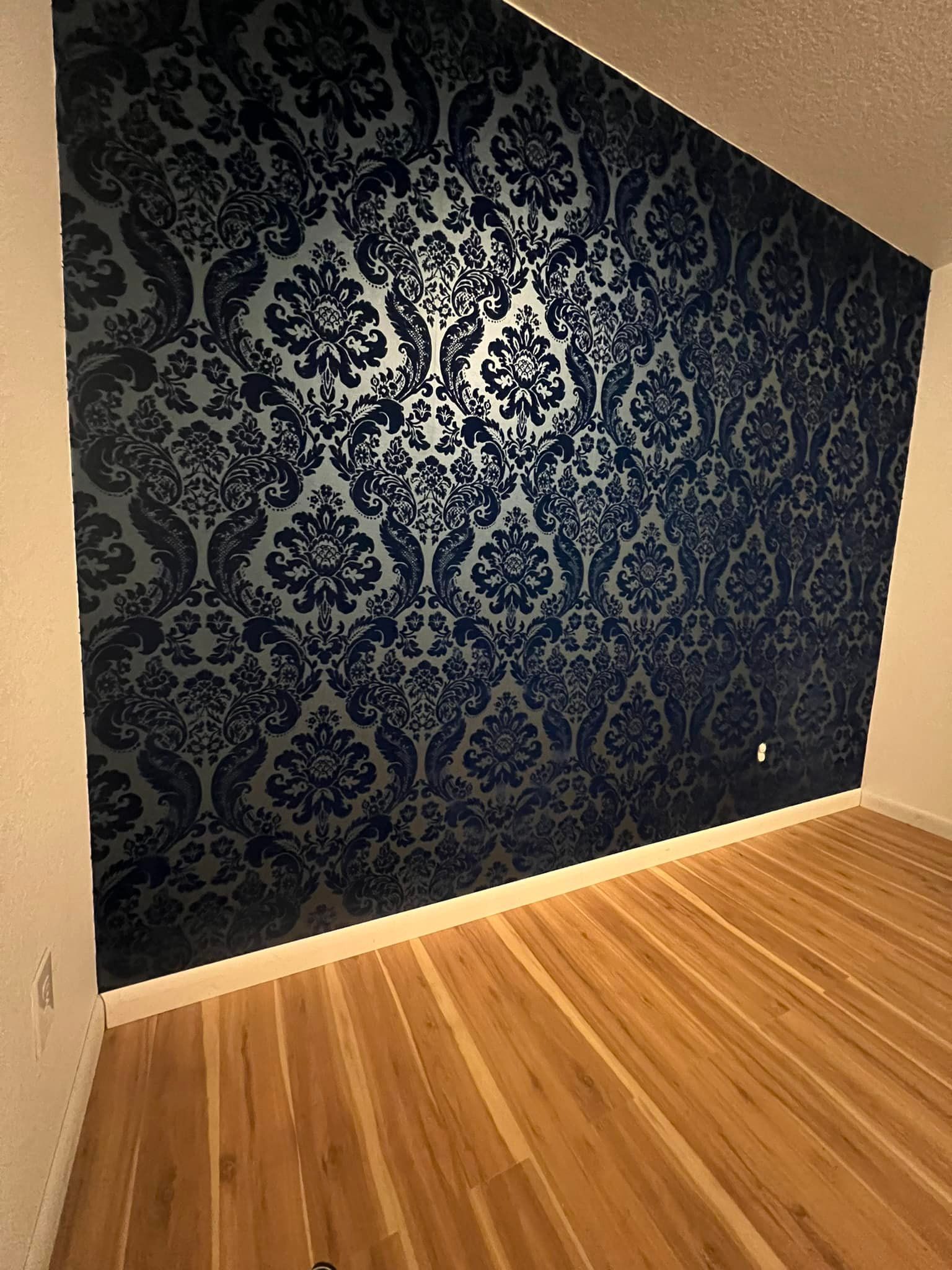 A room with hardwood floors and a dark blue floral wallpaper accent wall. The walls are a light cream color.
