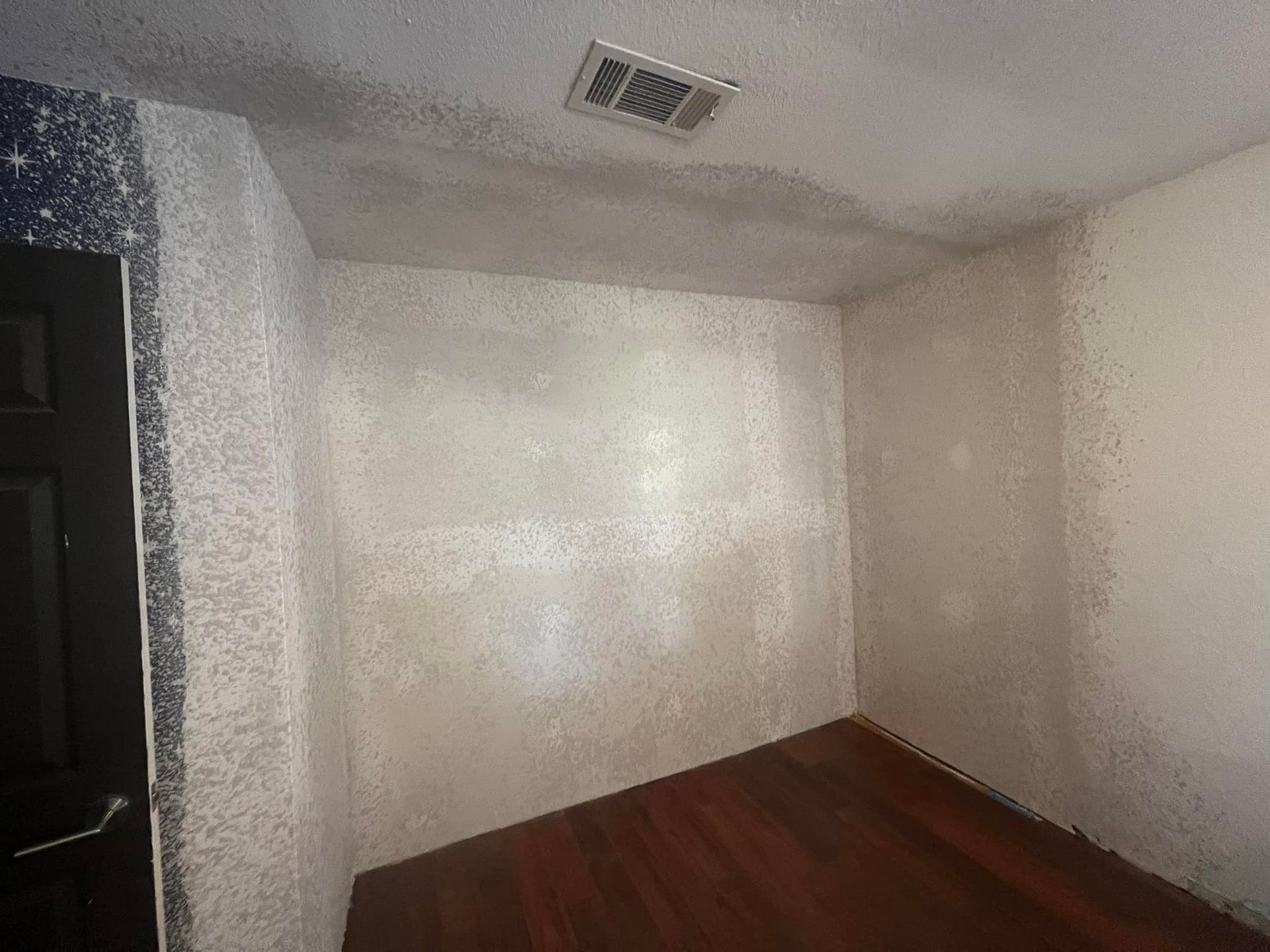 Empty interior room with dark wood floors, textured white walls, and a ceiling vent. A dark doorway is visible on the left.