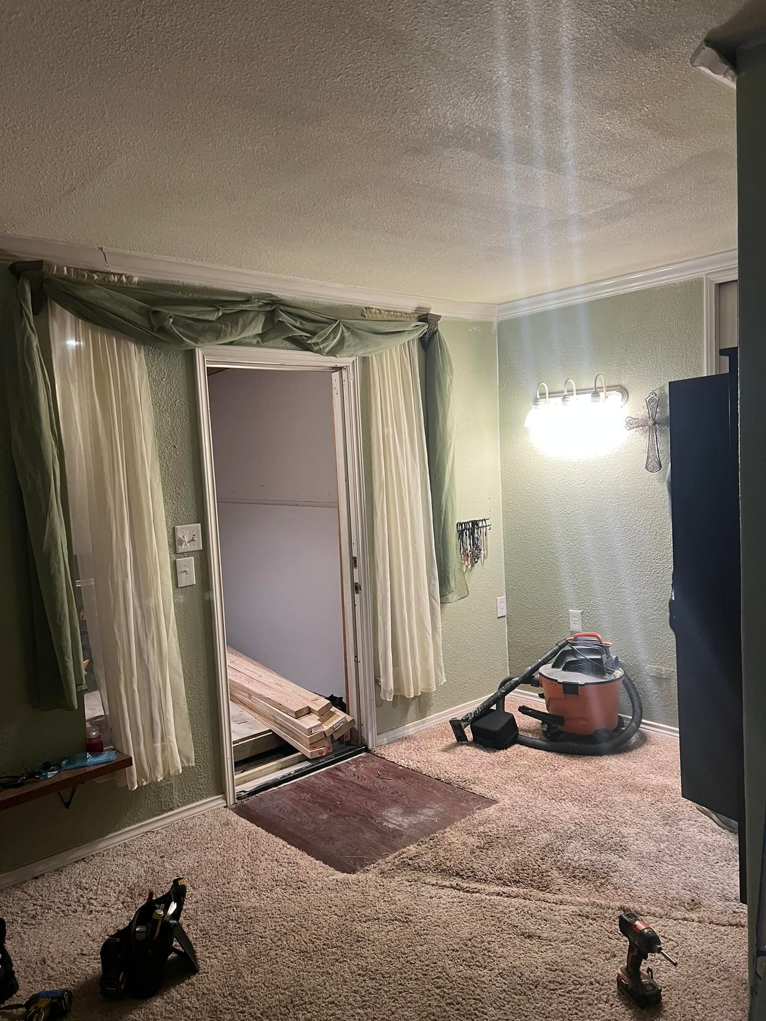 Interior view of a room with a door, rug, vacuum cleaner, and beige carpeting.