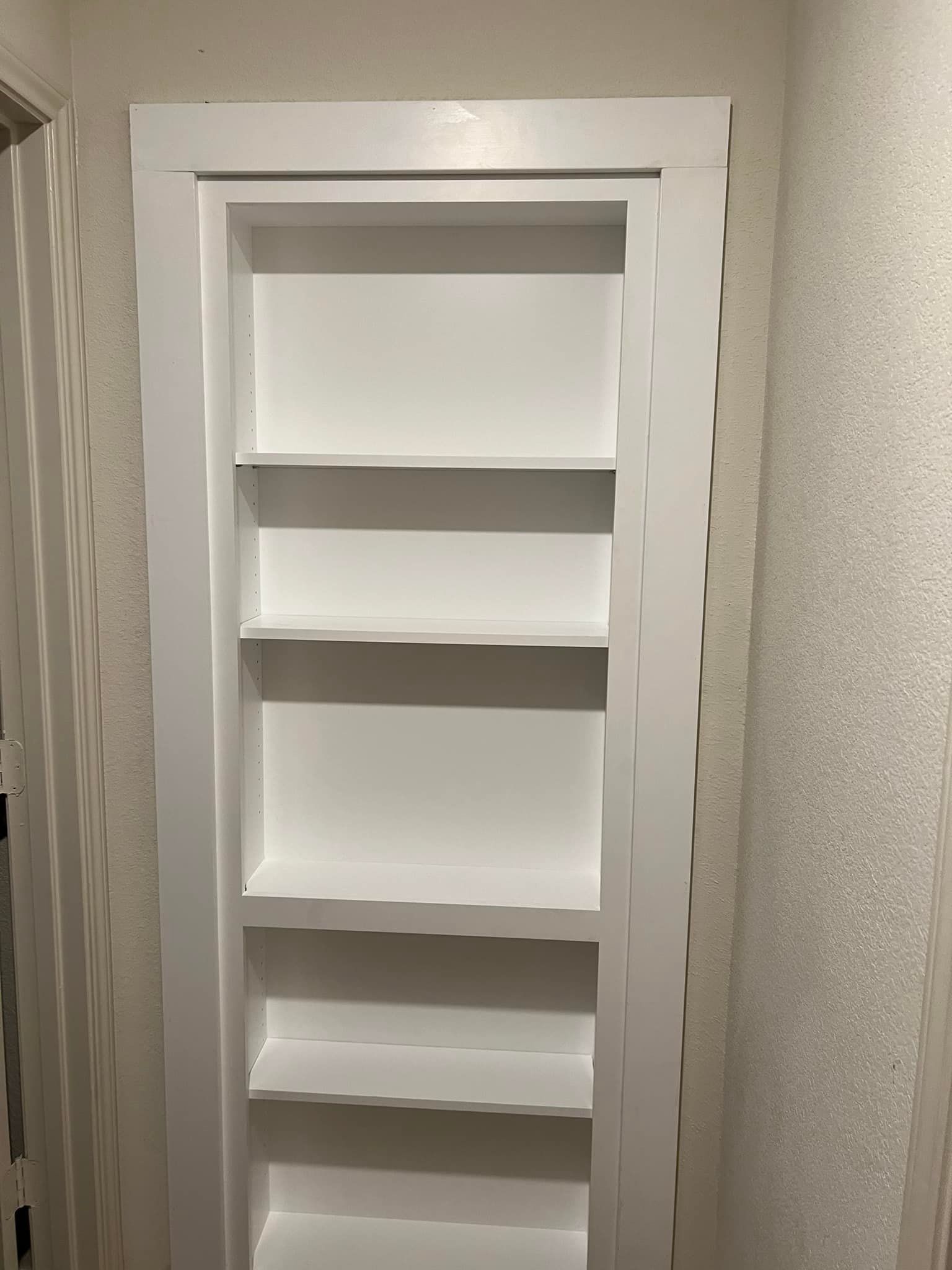 White built-in bookshelf with five shelves set into a wall. The shelves and surrounding trim are white.