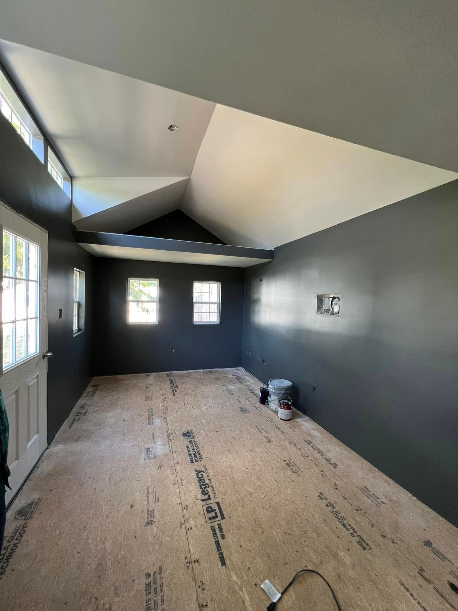An empty room with dark gray walls and a light wood floor, featuring a slanted white ceiling and multiple windows.