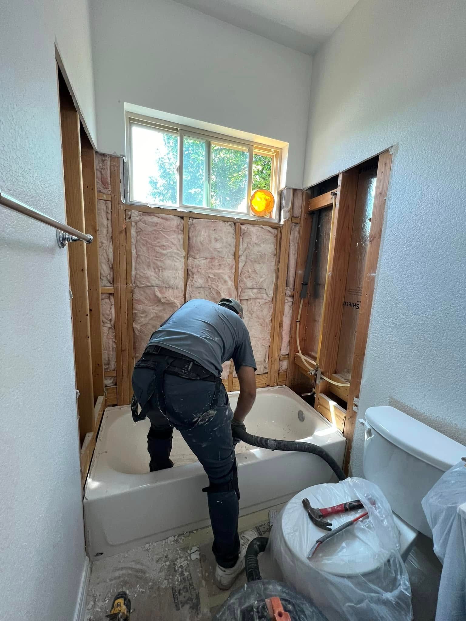 A person works on a bathroom renovation, vacuuming debris from a bathtub. 
