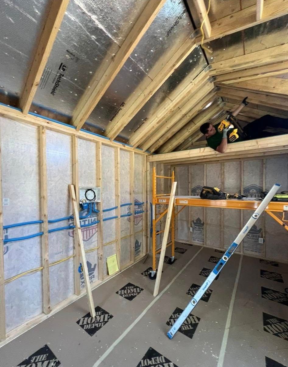 Interior view of a room under construction. The walls and roof are framed with wooden beams, covered with insulation.