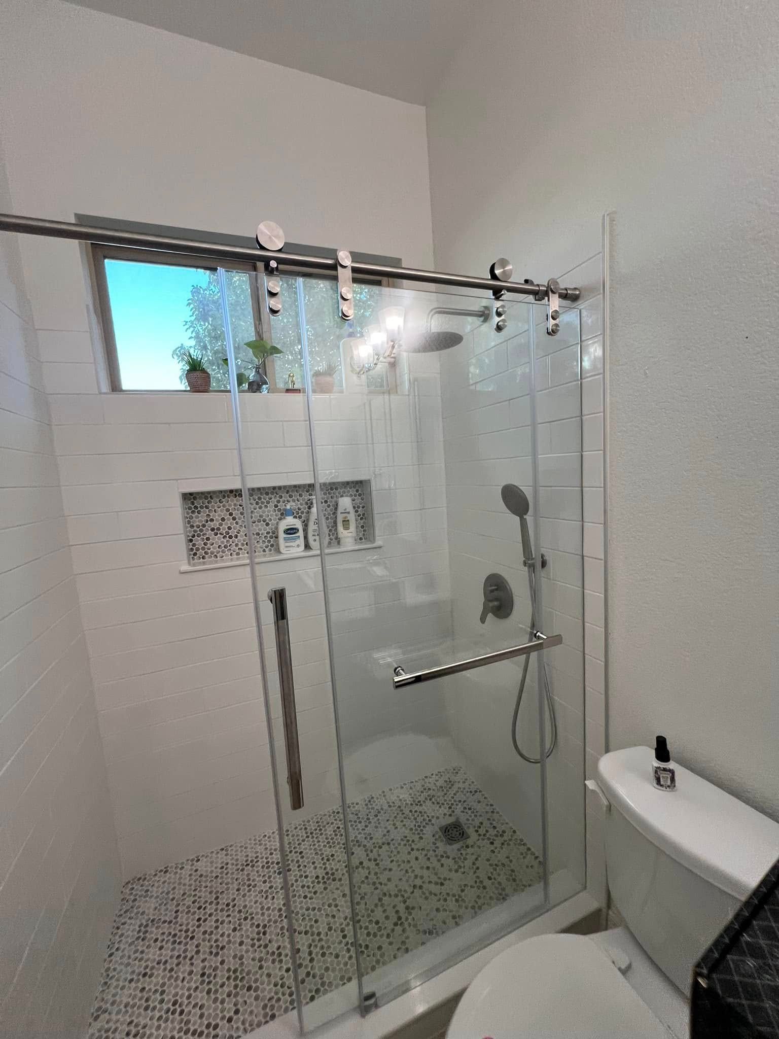 A modern bathroom with a glass shower, toilet, and white walls. The shower has a sliding door and a built-in niche.