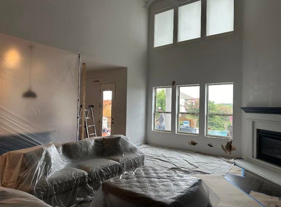 Living room covered in plastic sheeting during renovation, with tall windows, a fireplace, and sofa.