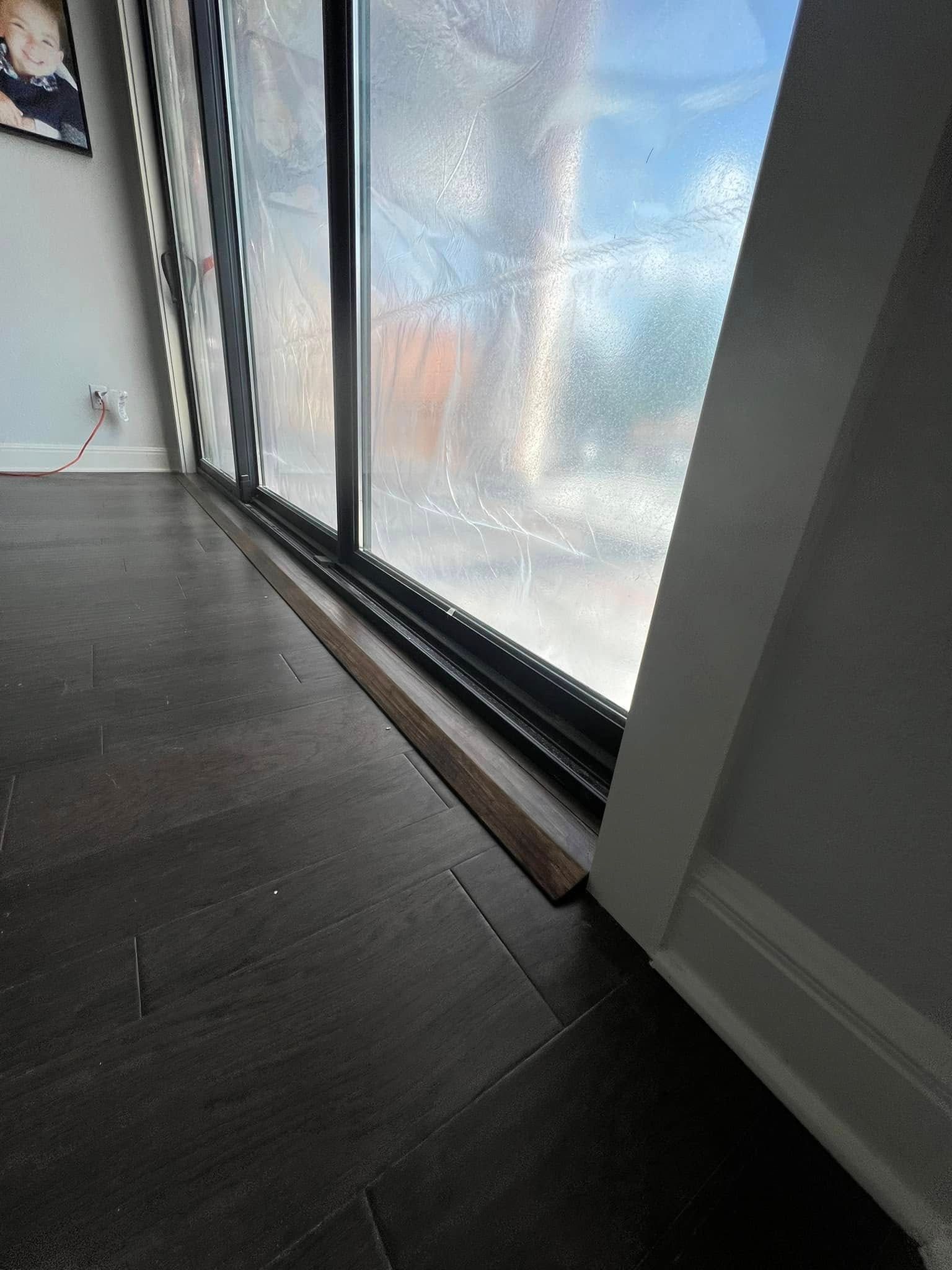 Dark tiled floor with a brown wooden strip in front of a large window. White trim is on the right side of the window.