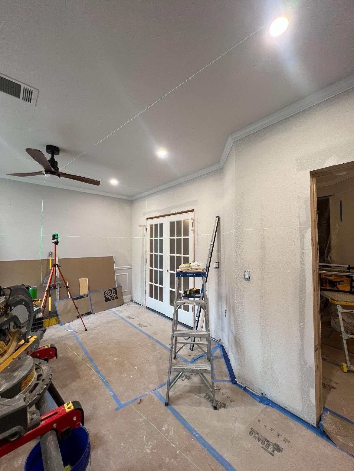 Interior room renovation in progress with French doors, crown molding, and construction tools. 