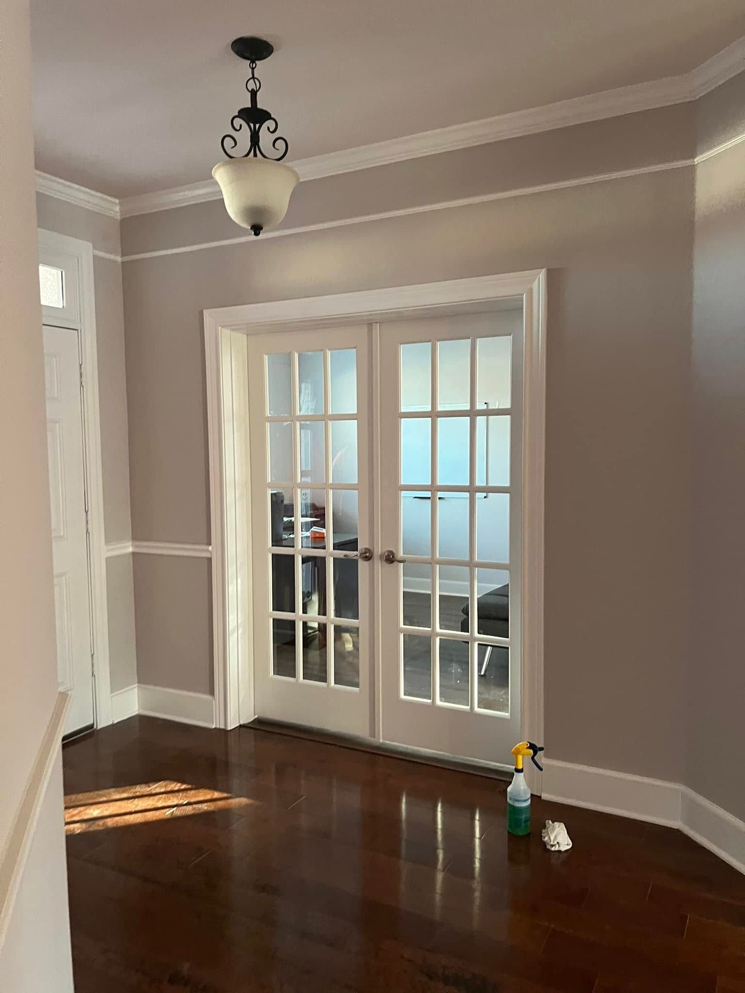 Interior view of a room with dark wooden floors, light gray walls, white trim, and french doors. 