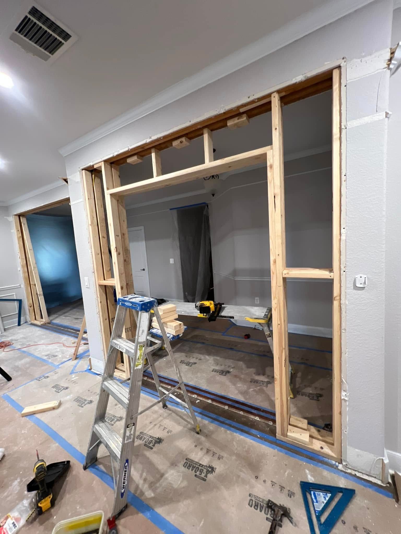 Interior framing of an open doorway under construction; a ladder is in the foreground, tools scattered about.